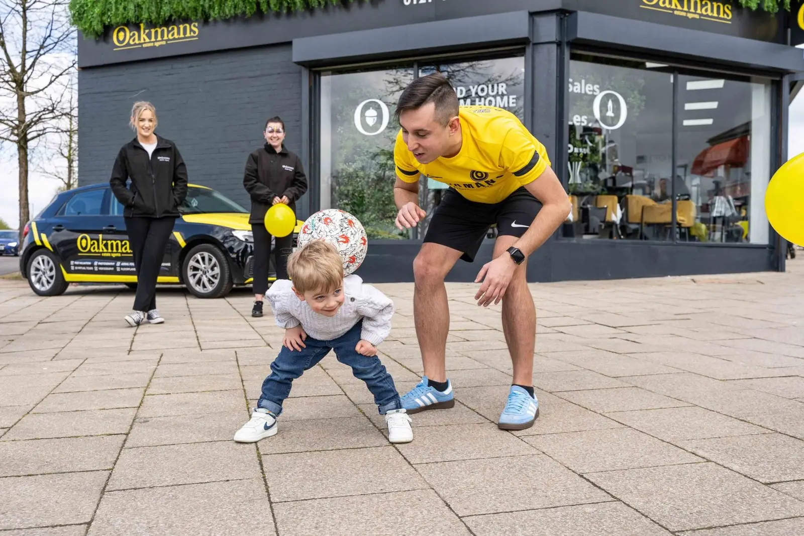 Football freestyler engaging with young child outside Oakmans estate agent during community event
