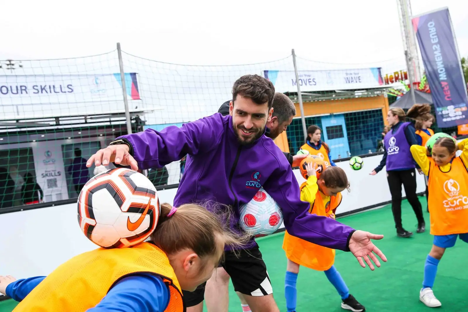 Freestyle football coach leading session with young girls wearing orange bibs at outdoor event